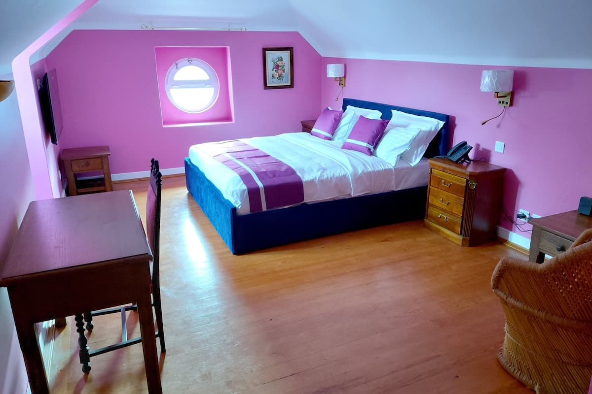 Une chambre à coucher comprenant un lit, un bureau, une chaise, une commode, une fenêtre et une lampe fixée au mur.