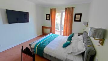 Quarto com cama, mesa de cabeceira, luminária na parede e janela com cortinas.