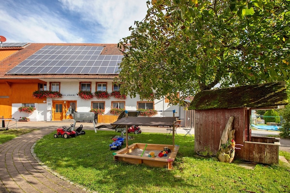 A house with solar panels, a garden, a play area, and a wooden structure.