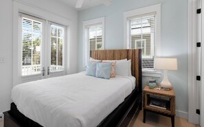 A bedroom with a large bed, white walls, and multiple windows with blinds.