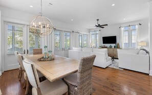 A spacious living room with a wooden dining table, white sofas, and a large TV.