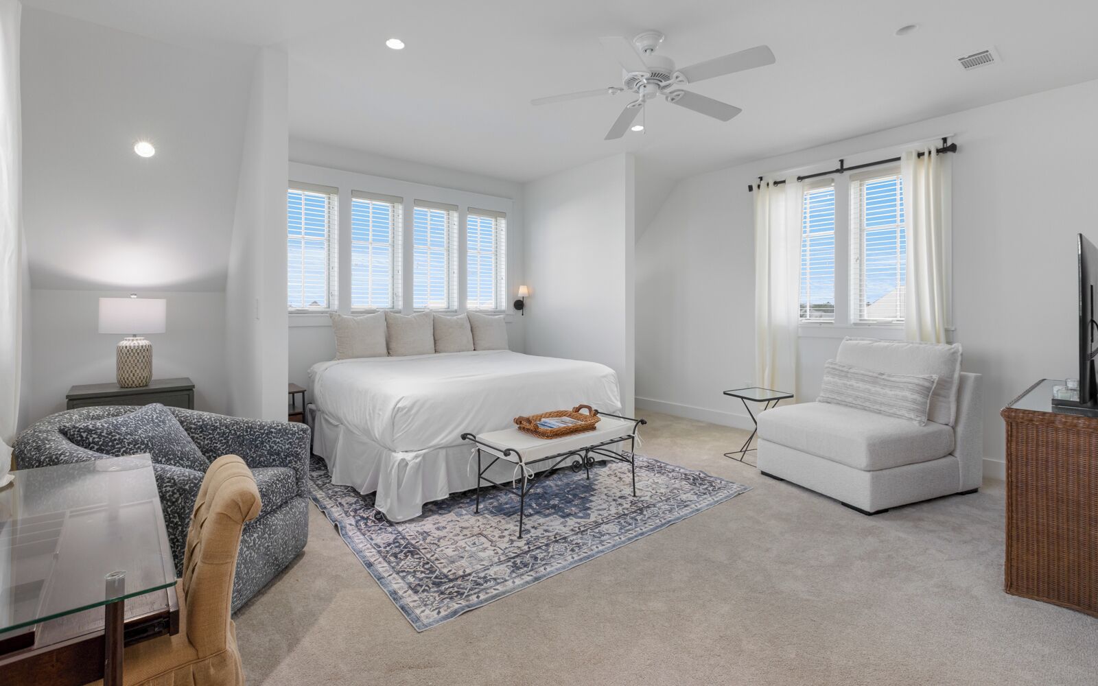 A modern bedroom with a large bed, a sitting area with a chair, a small table, and a ceiling fan.