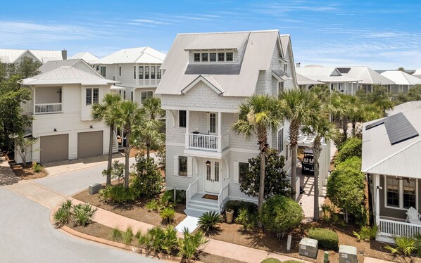 A multi-story residential building with a balcony, surrounded by palm trees and a well-maintained lawn.