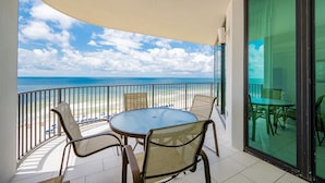 A balcony with a round table and chairs, overlooking a beach and ocean. - Phoenix Ix 907 2 Bedroom Condo (Orange Beach)