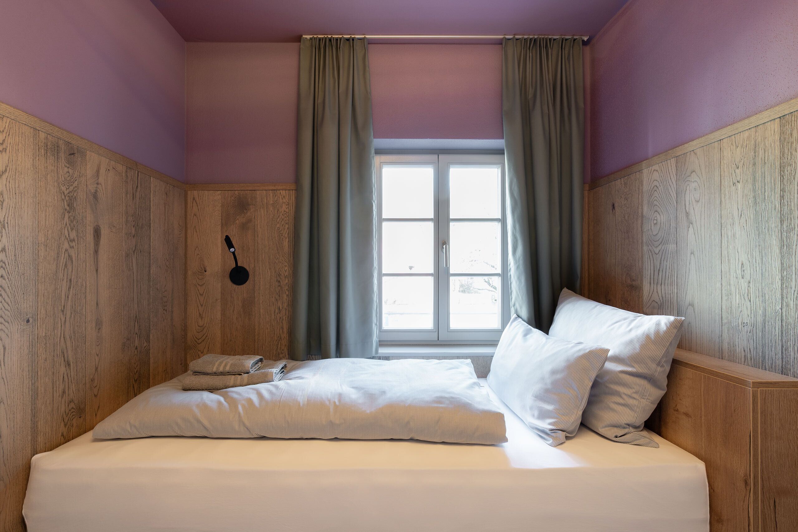 Un dormitorio con cabecera de madera, cama con ropa de cama blanca, mesita de noche y ventana con cortinas.