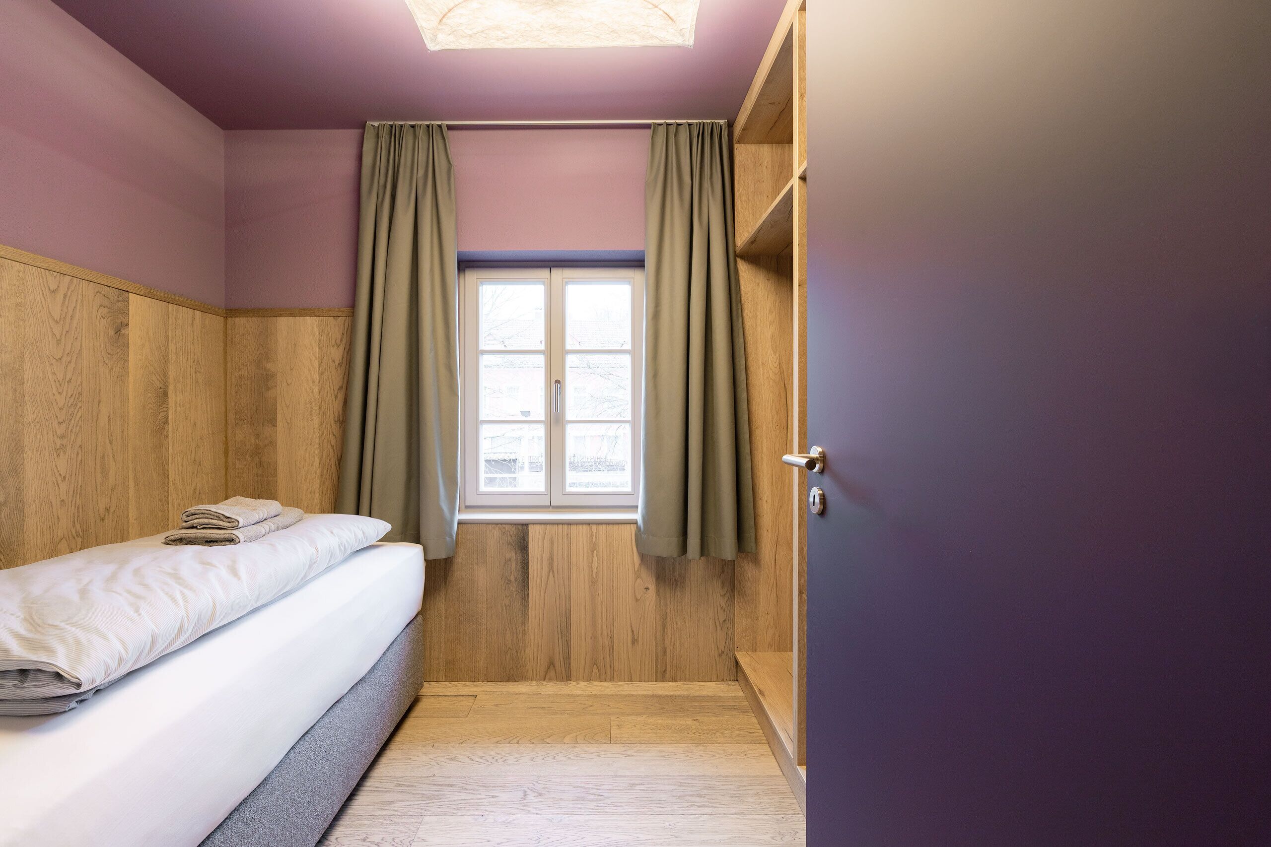 Una habitación pequeña con una cama, una ventana con cortinas y una puerta.