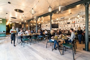A restaurant with multiple tables and chairs, a waiter serving food, and shelves with various items in the background.