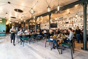 Ein Restaurant mit mehreren Tischen und Stühlen, ein Kellner serviert Speisen, im Hintergrund Regale mit verschiedenen Gegenständen.