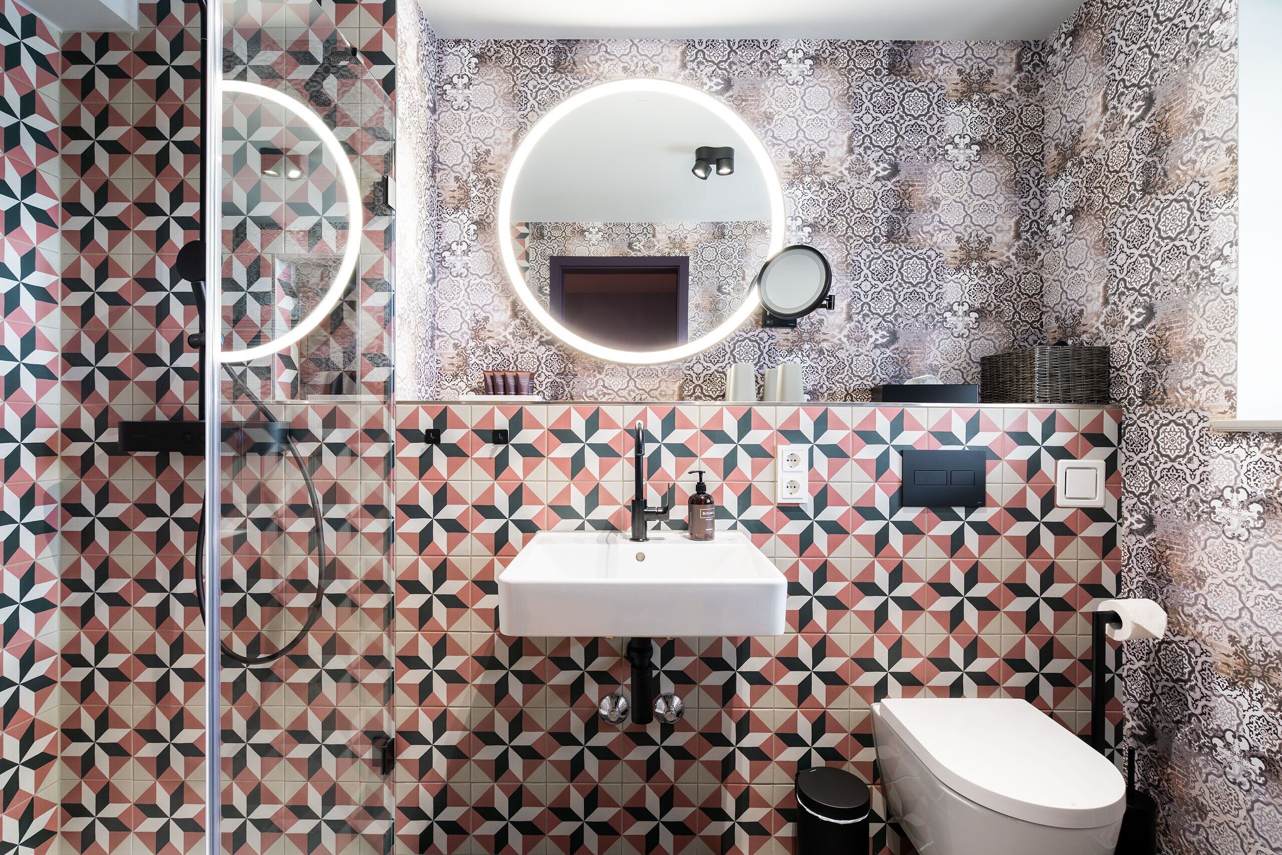 A bathroom with a geometric patterned wall, a white sink, a mirror, and a toilet.