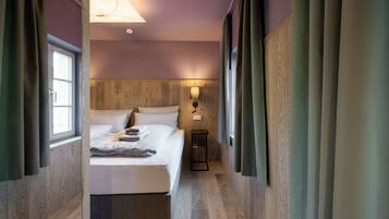 Habitación de hotel con cabecera de madera, cama con sábanas blancas, mesita de noche y lámpara de pared.