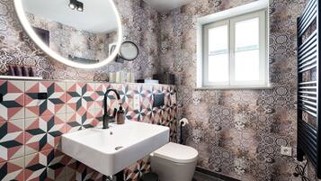 A bathroom with patterned tiles, a white sink, a toilet, a mirror, and a window.