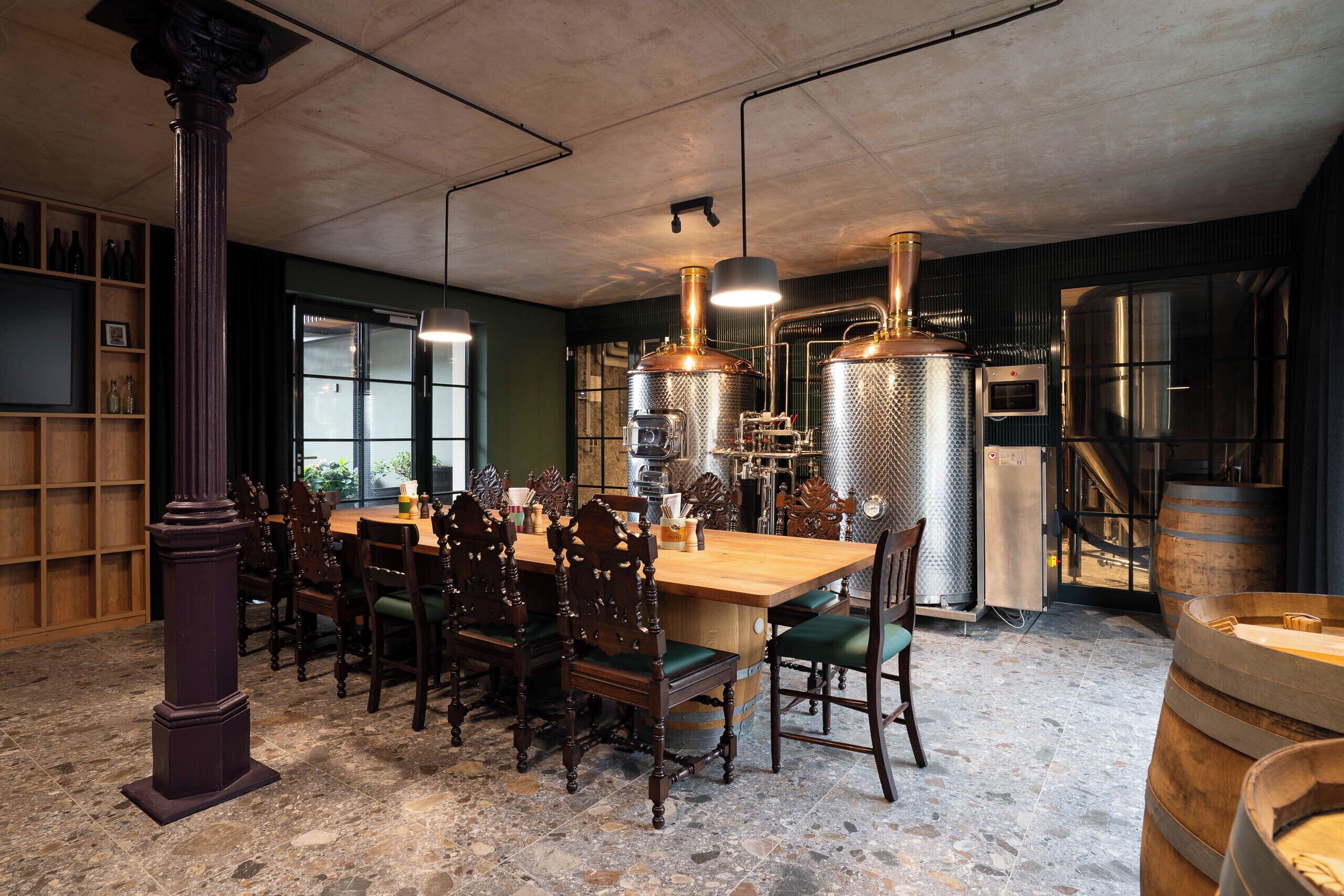 A dining area with a wooden table and chairs, a large column, and industrial-style brewing equipment.