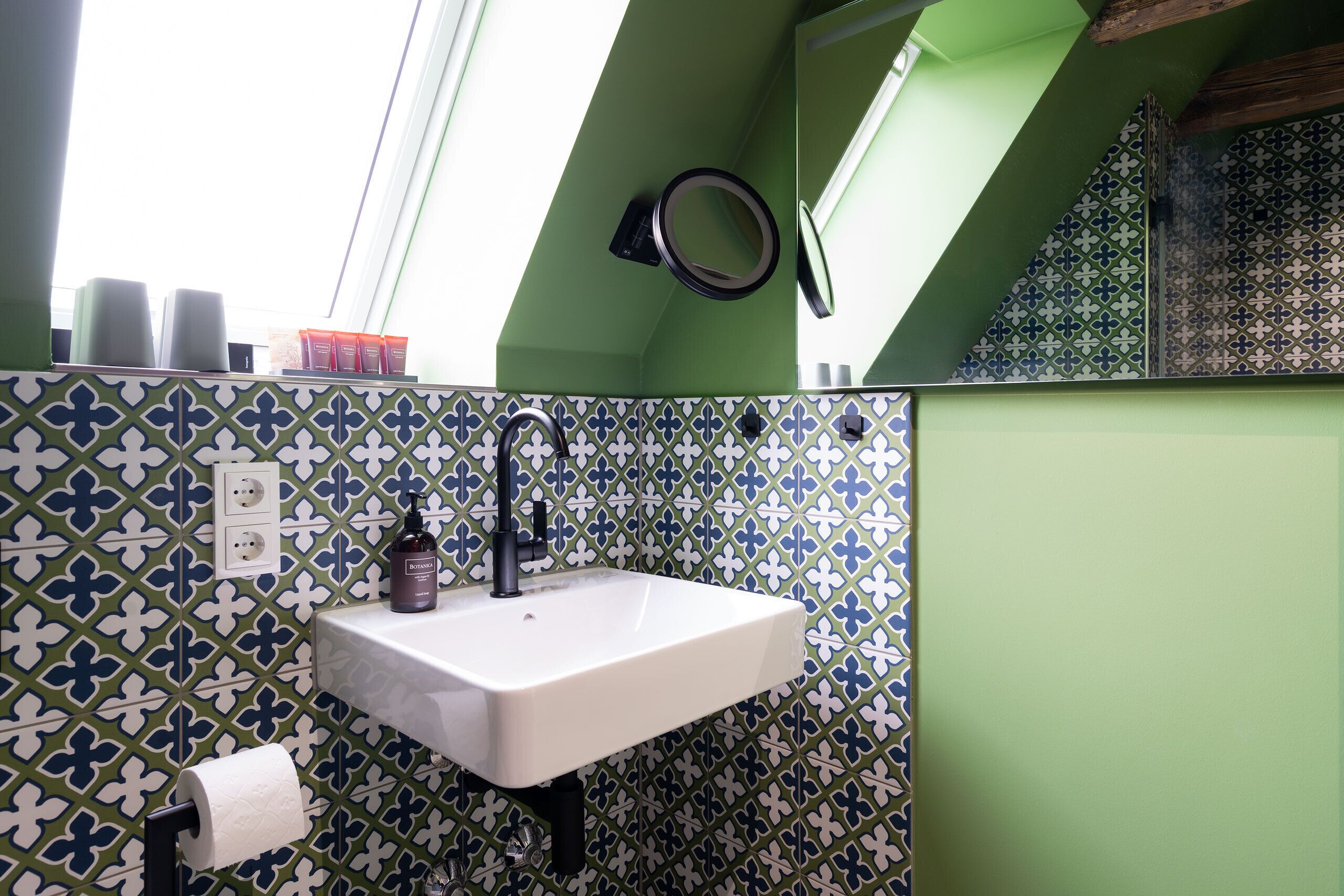 Un bagno con un lavandino bianco, pareti verdi e piastrelle decorate.