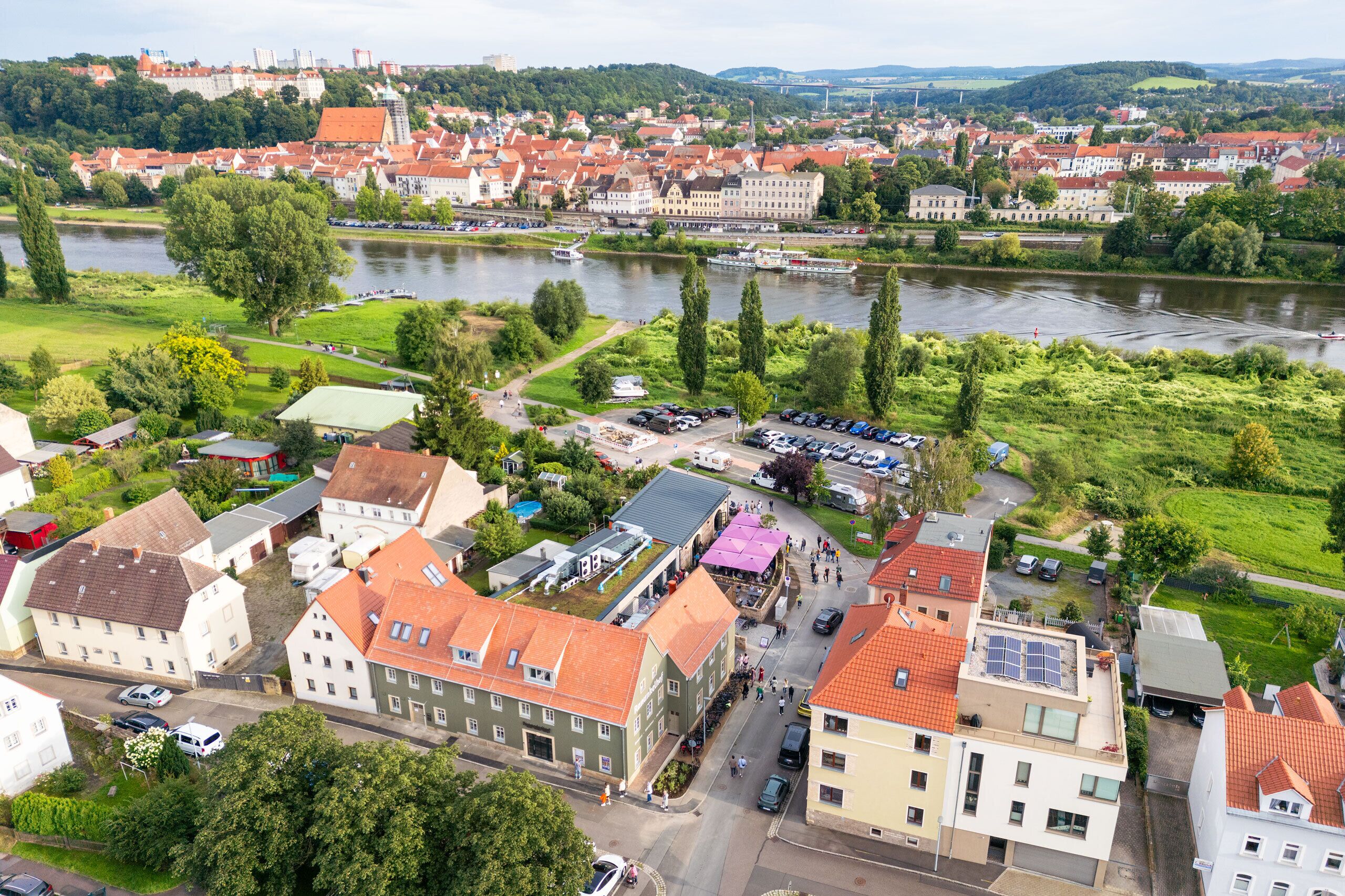 A riverside town with historic buildings, a river, and a park.