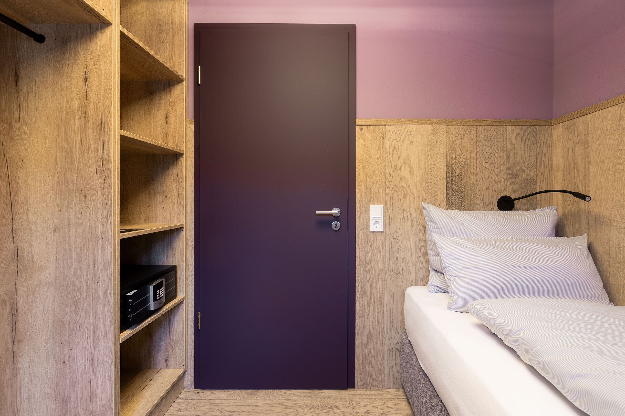 A compact room with a wooden wardrobe, a bed with white bedding, and a purple door.