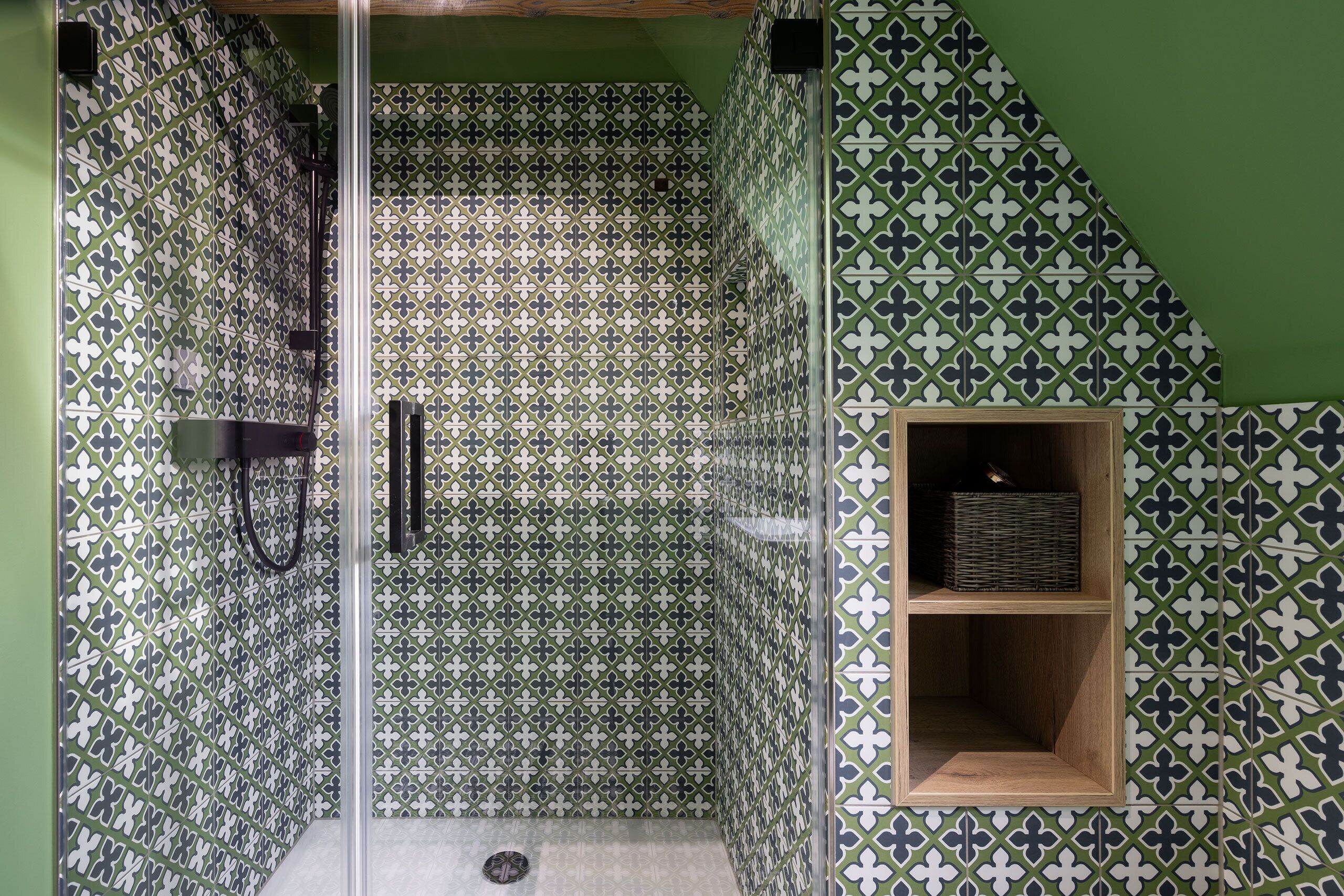 A shower with a glass door, a wooden shelf, and patterned tiles.