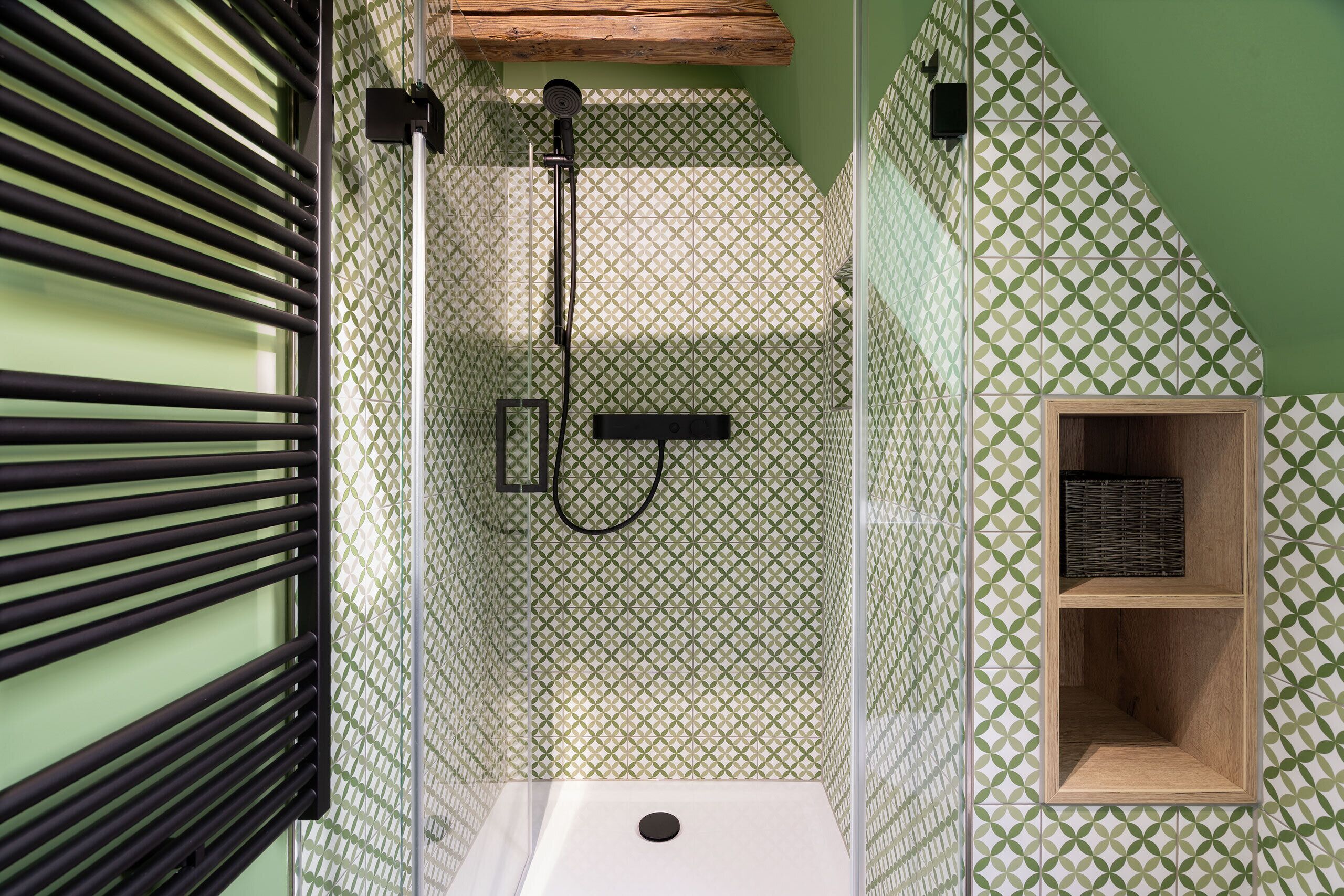 A shower with a geometric patterned wall, a wooden shelf, and a black faucet.