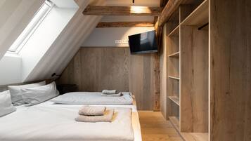 A bedroom with a sloped ceiling, wooden beams, a flat-screen TV, and a bed with neatly folded towels.
