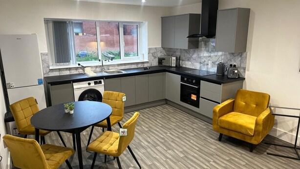 A modern kitchen with grey cabinets, a black range hood, and a window overlooking a brick wall. - Chapel Rise Apartments (Long Eaton)