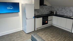 A modern kitchen with white cabinets, a black countertop, a built-in oven, and a microwave. - Chapel Rise Apartments (Long Eaton)
