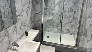 A modern bathroom with a glass shower enclosure, marble walls, and a white sink. - Chapel Rise Apartments (Long Eaton)