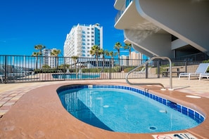 Una piscina con borde curvo, rodeada de una valla y palmeras al fondo.