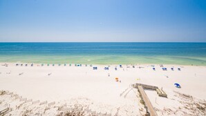 A beach with a wooden boardwalk leading to the water, clear skies, and beach umbrellas.