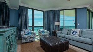 Un salon avec vue sur l’océan, un canapé, deux fauteuils à motifs, une table basse et un meuble.