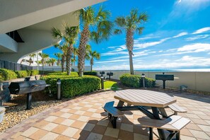 A patio area with a picnic table, grill, and palm trees. - Phoenix Ix 705 3 Bedroom Condo (Orange Beach)