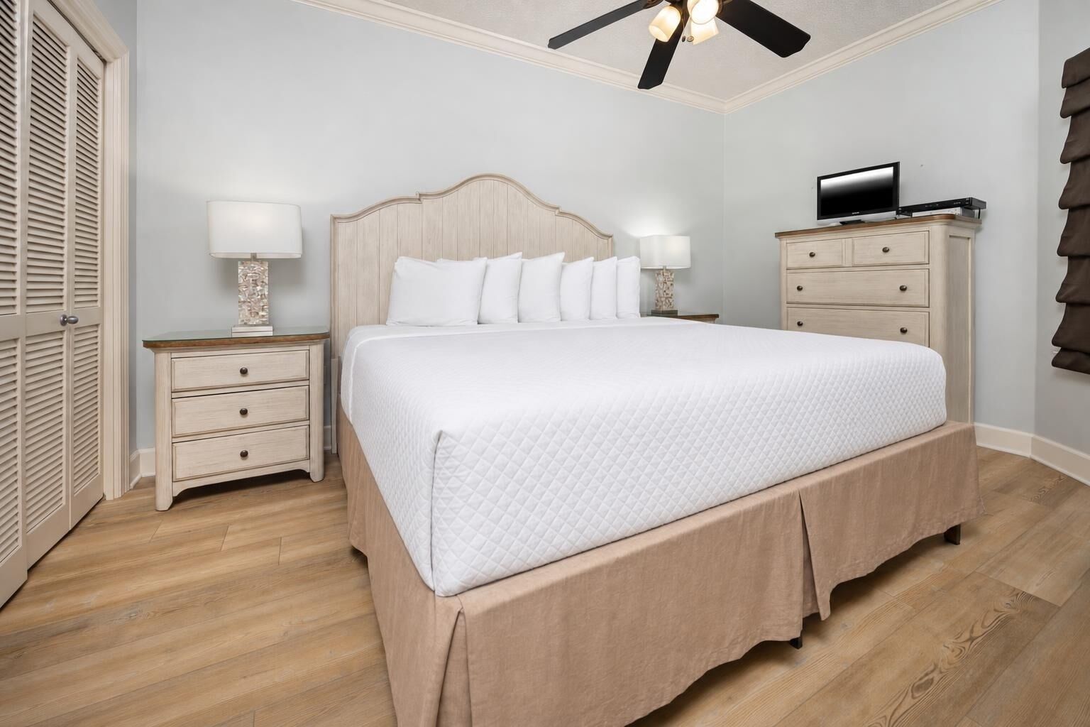 A bedroom with a bed, a nightstand, a dresser, a ceiling fan, and a television.