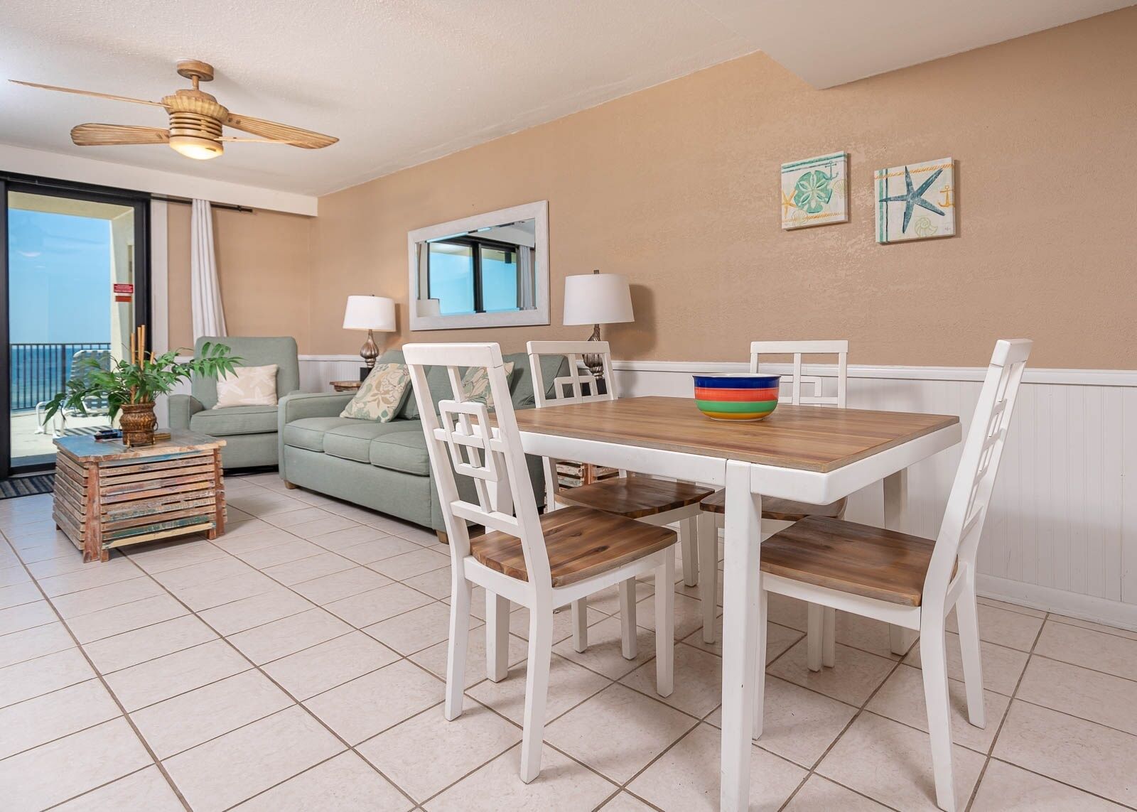 A dining area with a wooden table and white chairs, a green sofa, and a ceiling fan.