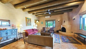 Un salón amplio con chimenea, vigas de madera en el techo y un ventanal que deja entrar luz natural.