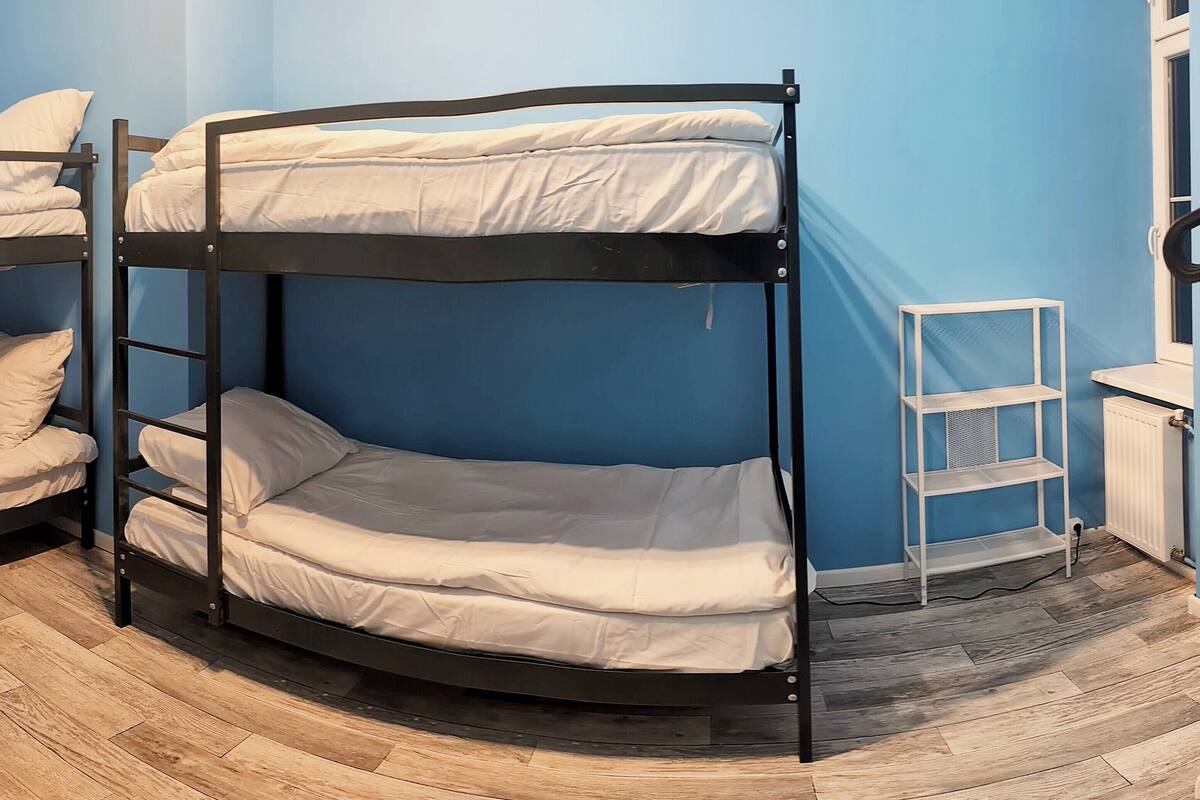 A bunk bed room with a wooden floor, a white metal shelf, and a radiator.