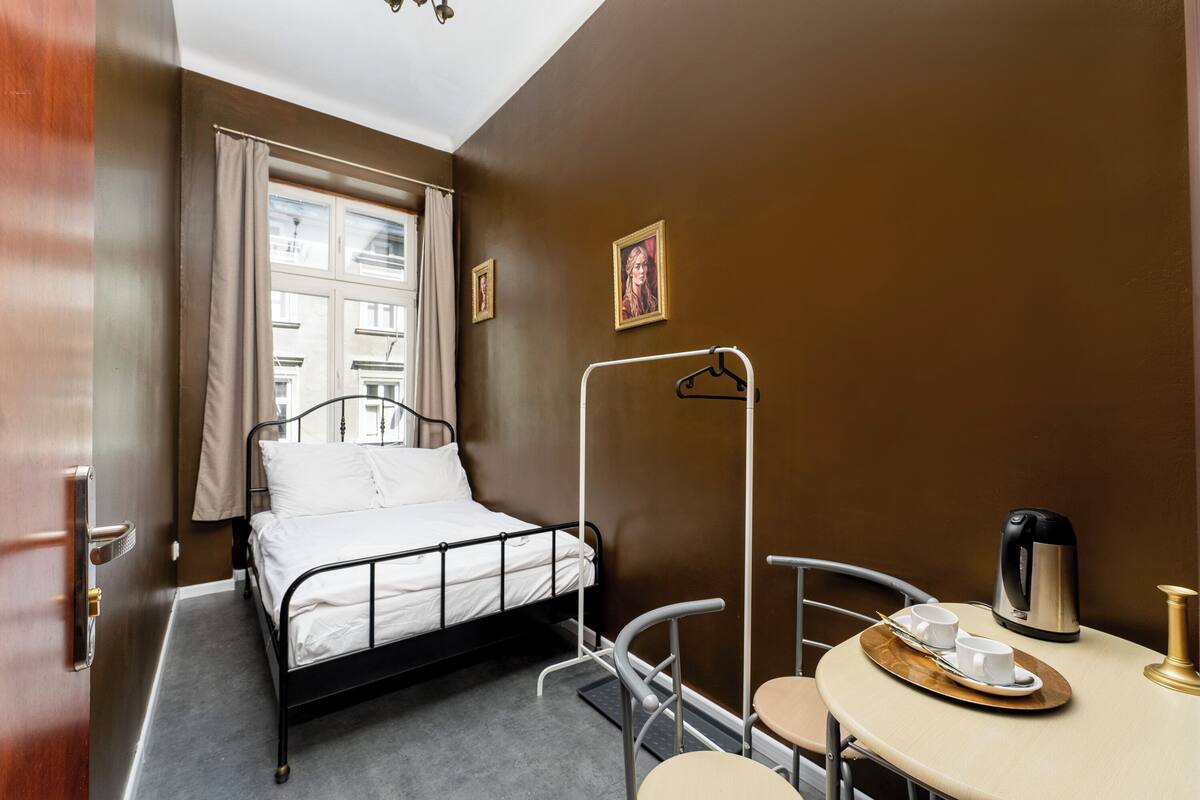 A hotel room with a single bed, a small table with a tray of cups and a kettle, and a chair.