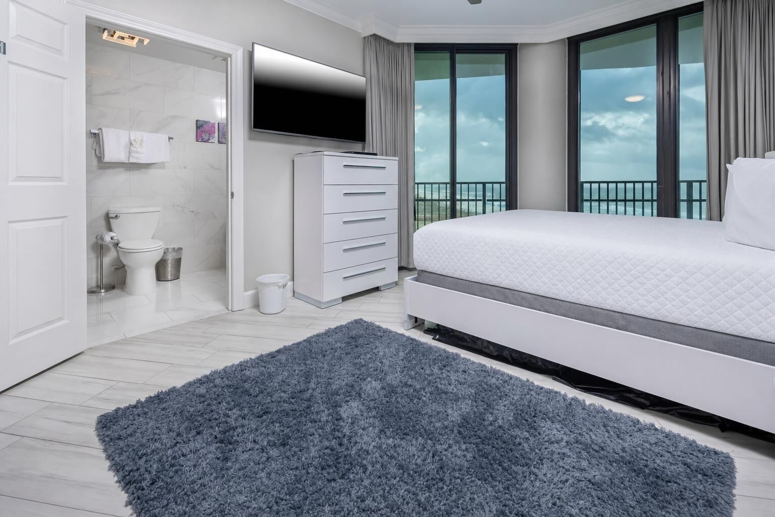 Un dormitorio moderno con una cama grande, un armario, un televisor y un balcón con vistas.