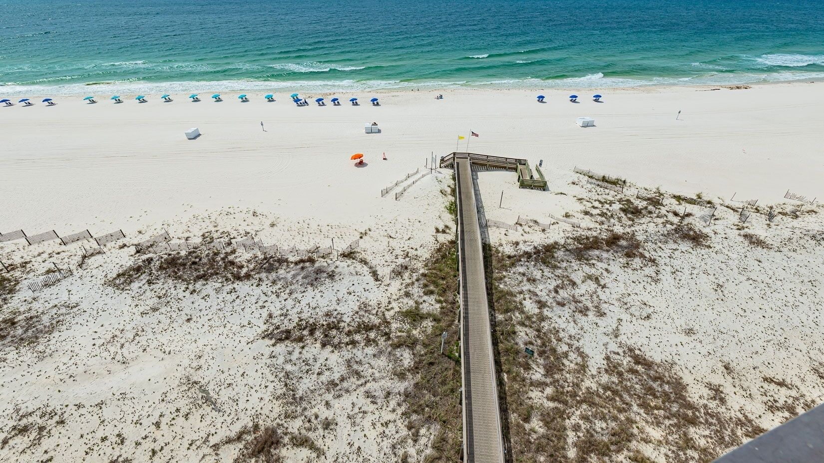 A beach with a wooden boardwalk leading to the water, lined with beach umbrellas.