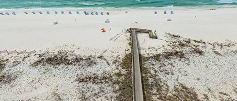 A beach with a wooden boardwalk leading to the water, lined with beach umbrellas.