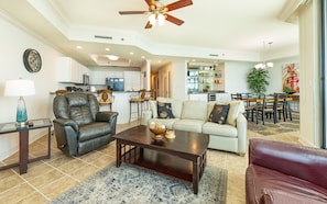 A living room with a sofa, a coffee table, a leather armchair, and a dining area with a table and chairs. - Phoenix Ix 1506 2 Bedroom Condo (Orange Beach)