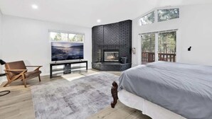 Une chambre moderne dotée d’un grand lit, d’une télévision, d’une cheminée et offrant une vue sur l’extérieur.