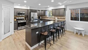 Une cuisine moderne avec un îlot central, des tabourets de bar et une table à manger près d’une fenêtre.