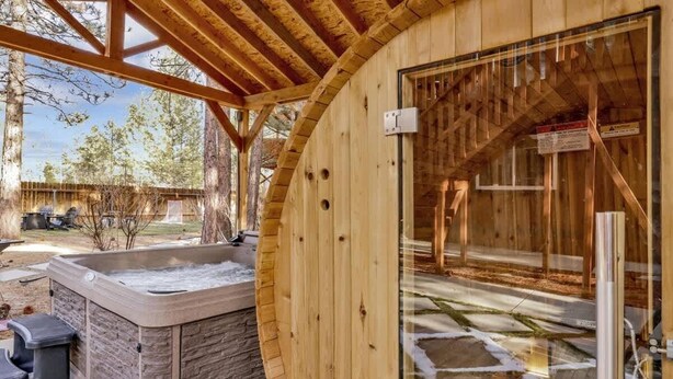 Une cabane en bois dotée d’un bain à remous, de murs en pierre et d’une porte en verre donnant sur un espace extérieur couvert.