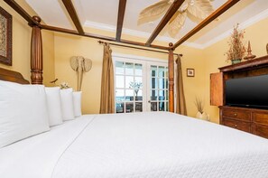 Un grand lit avec du linge de lit blanc, une tête de lit en bois, un téléviseur à écran plat et un balcon avec vue.