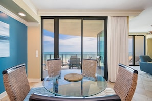 A glass-top table with wicker chairs, a view of the ocean through a sliding glass door, and a balcony with a blue chair. - Phoenix Ix 505 3 Bedroom Condo (Orange Beach)