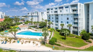 A modern hotel with multiple white buildings, a central pool area, and surrounding greenery.