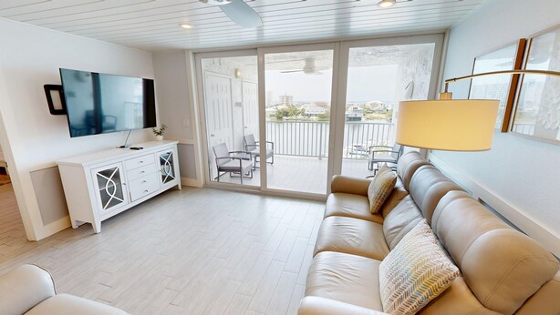 A modern living room with a sofa, a TV, a white cabinet, and a balcony with outdoor furniture.