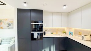 Una cocina moderna con armarios oscuros, horno empotrado y encimera con fregadero y tostadora.
