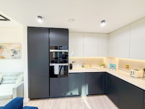 Una cucina moderna con mobili scuri, forno integrato e un piano di lavoro con lavello e tostapane.