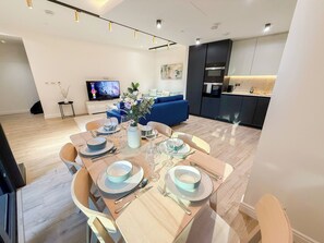 Un soggiorno moderno con zona pranzo, un divano blu, una cucina e una TV sullo sfondo.