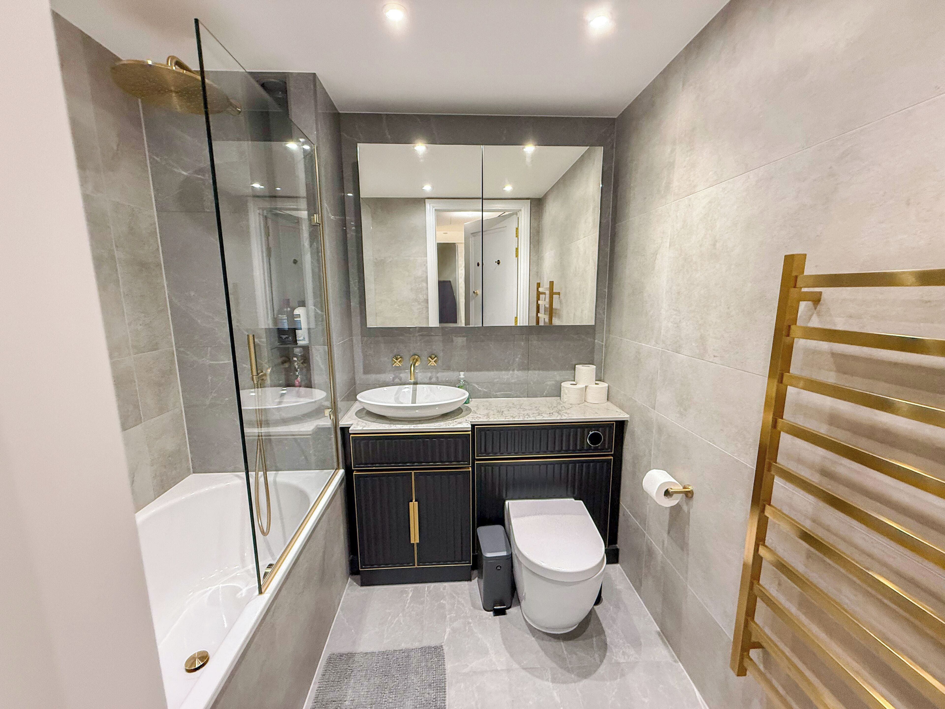 Ein modernes Badezimmer mit einer gläsernen Duschkabine, zwei Waschbecken, einer Toilette und einem Handtuchhalter.