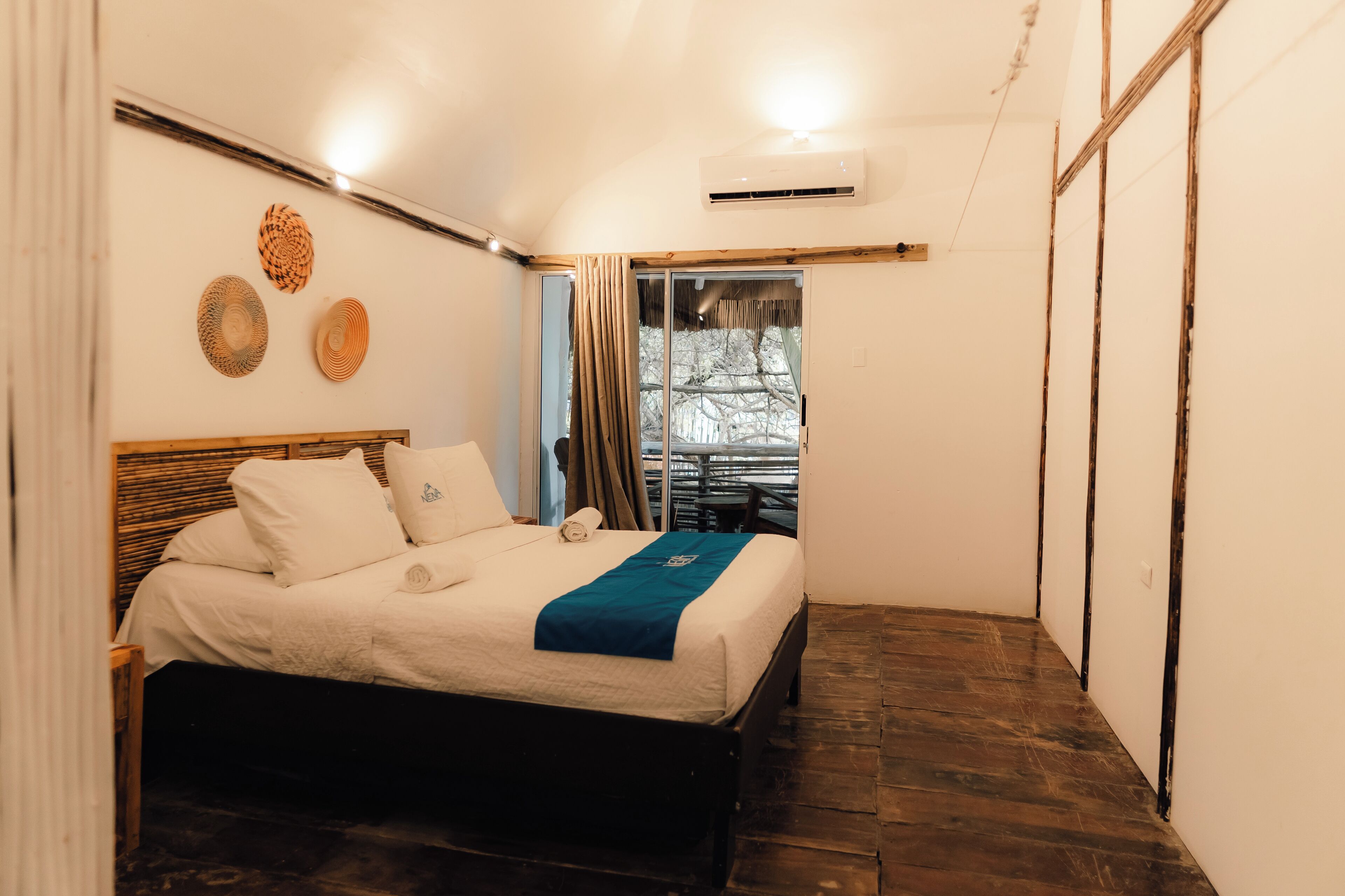 A small, cozy bedroom with a wooden bed, a window with curtains, and a view of trees outside.